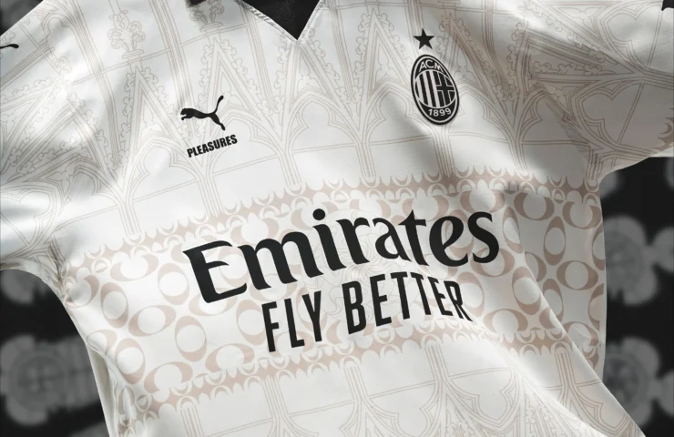 Gros plan sur un élégant maillot de football de l'AC Milan, blanc avec un motif graphique détaillé, sponsorisé par "Emirates Fly Better", avec un logo Puma noir et blanc et un col à motif noir.