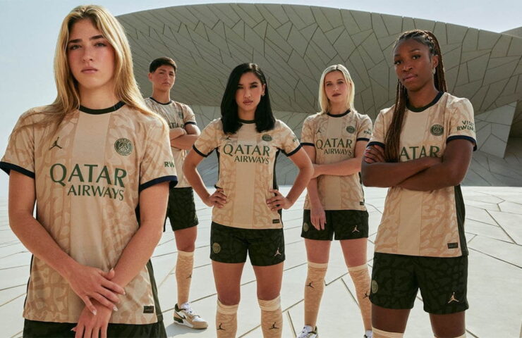 Group of football players presenting their team's beige jersey with 'Qatar Airways' as sponsor, standing in front of an architecturally complex building, exuding strength and team spirit.