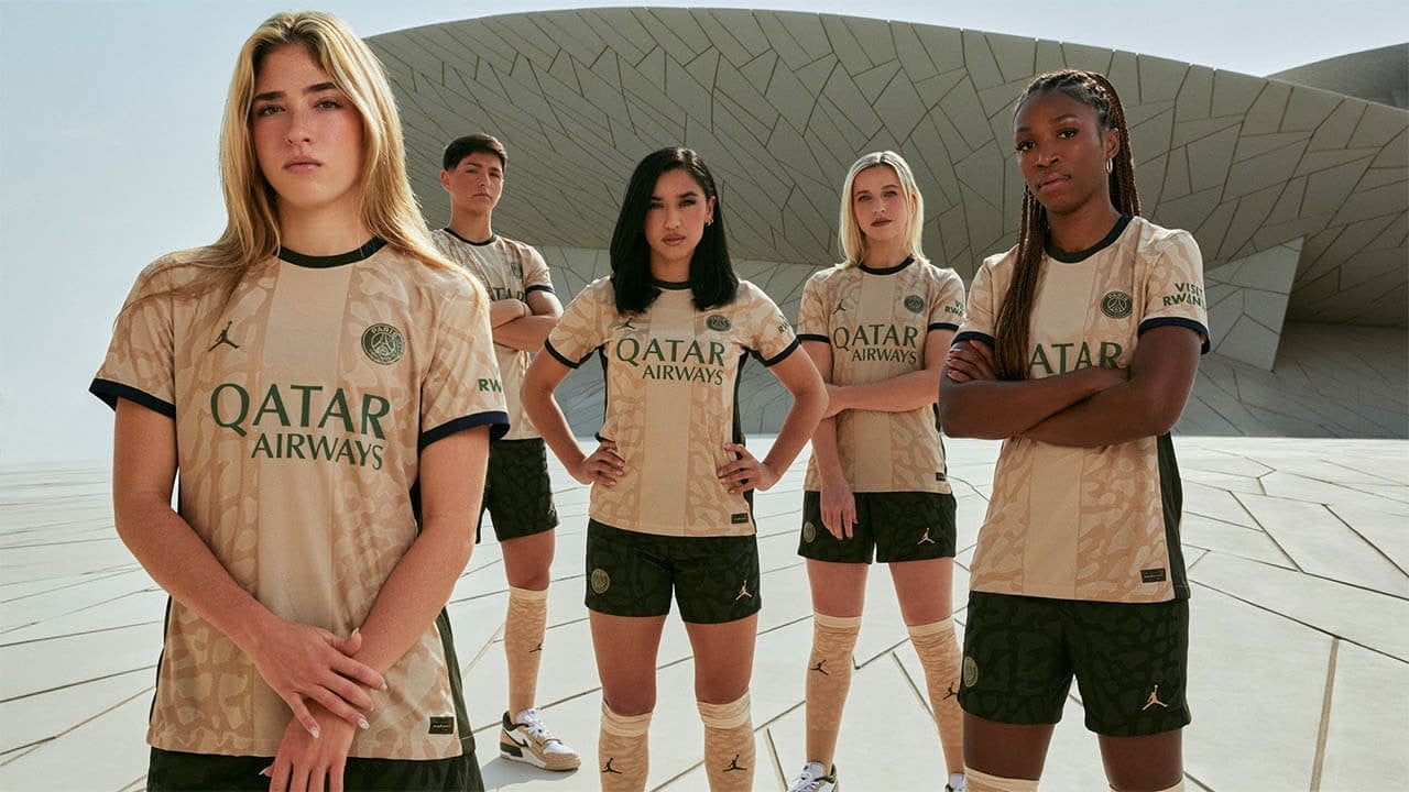 Group of football players presenting their team's beige jersey with 'Qatar Airways' as sponsor, standing in front of an architecturally complex building, exuding strength and team spirit.