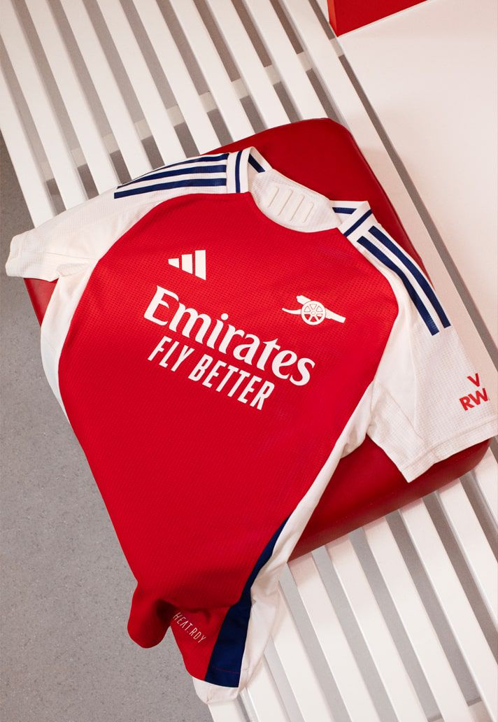 Le maillot domicile d'Arsenal 2024/2025 est étalé sur un banc rayé dans le vestiaire.